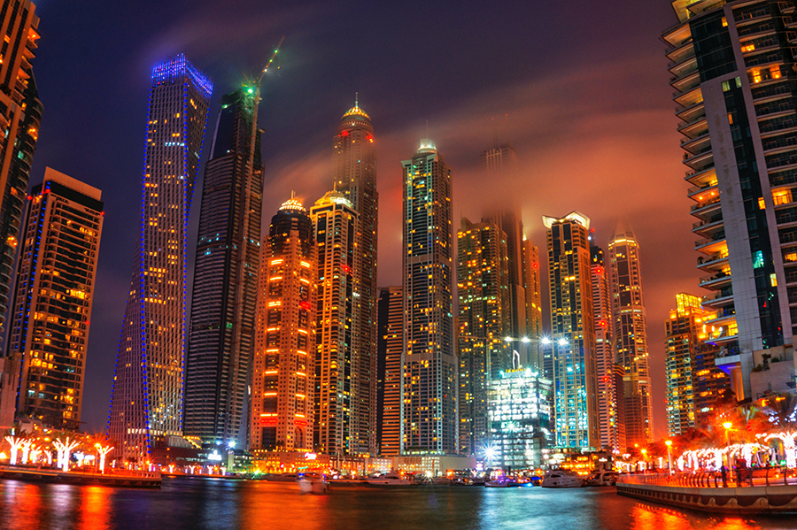 Night time city skyscrapers clustered around water and brightly illuminated.