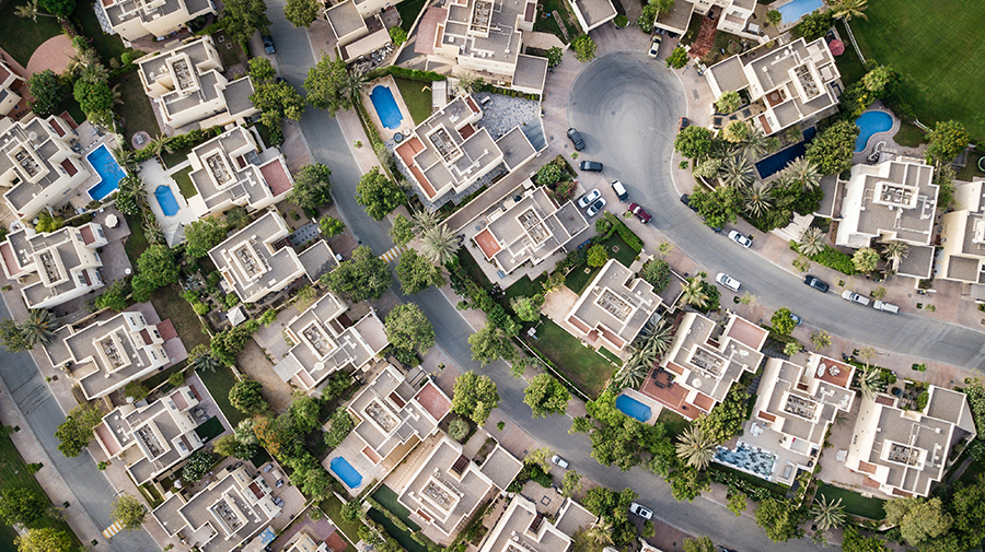 Aerial view of a housing estate with lush gardens and swimming pools.