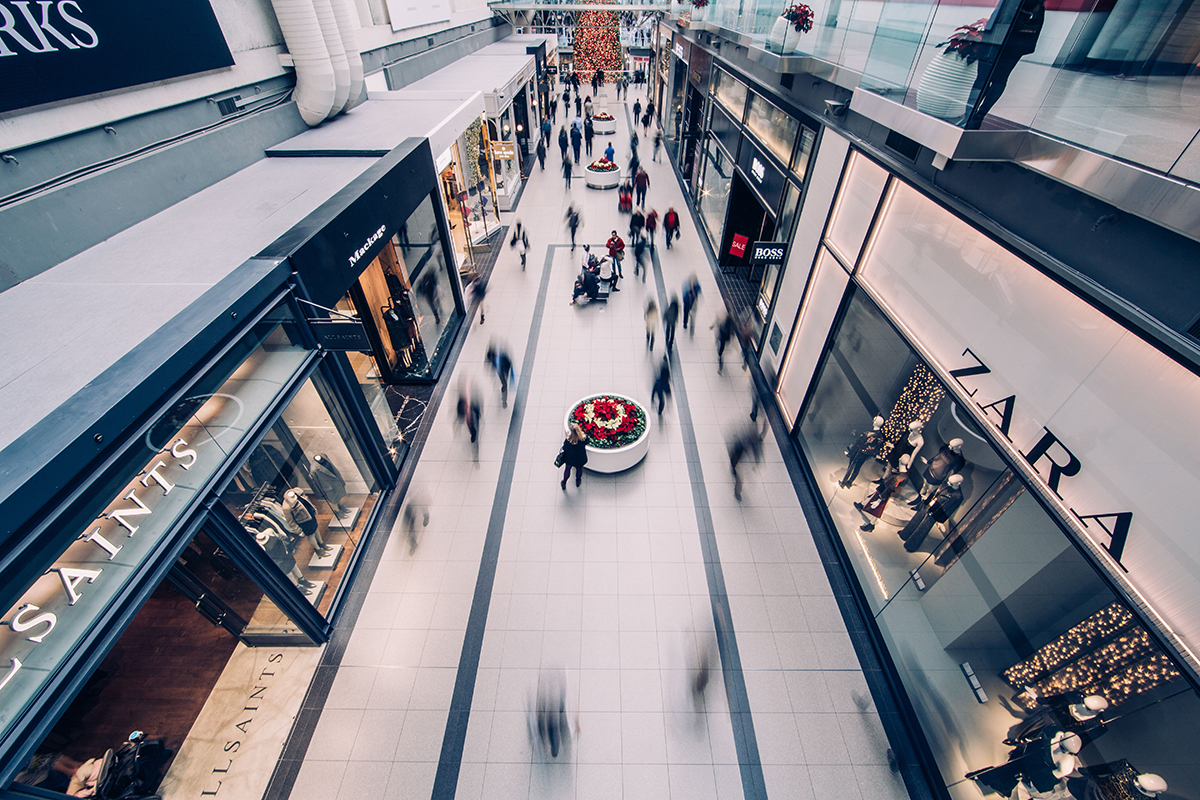 View from balcony down to a lower floor of a busy shopping centre with clothing stores on either side.