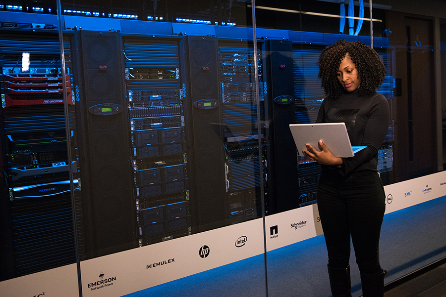 An engineer, holding a laptop while standing in front of server racks in data centre.